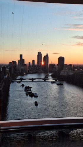 City skyline at sunset with river, boats, and bridge viewed from balcony - urban waterfront scene with golden hour lighting