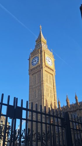 Big Ben clock tower at the Palace of Westminster in London with ornate Gothic architecture against clear blue sky