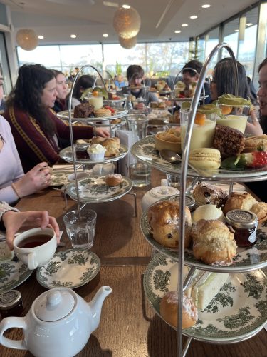 People enjoying traditional afternoon tea with tiered stands of scones, cakes, and sandwiches in elegant restaurant setting
